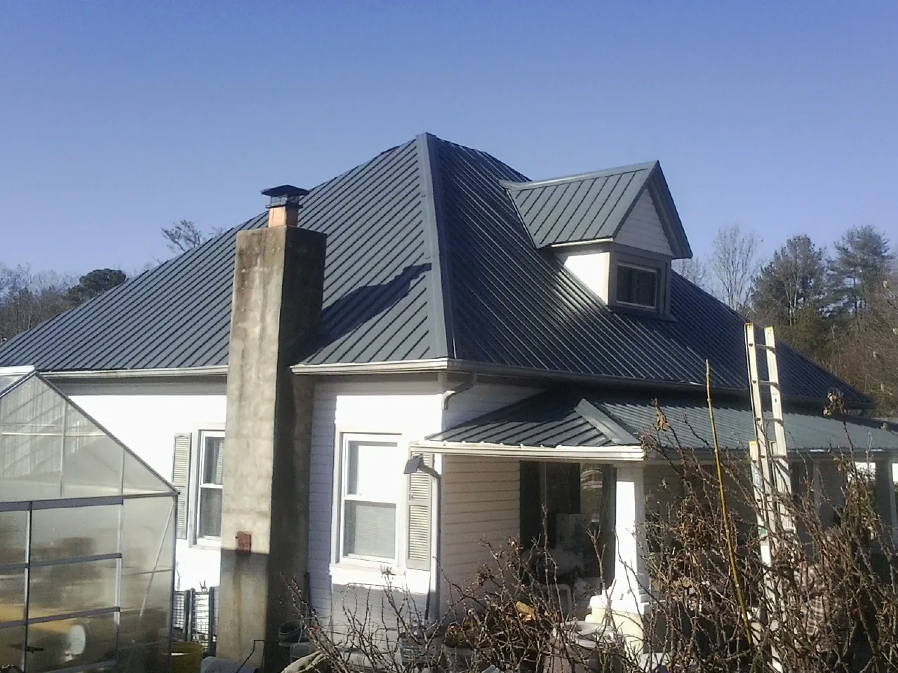 Dark blue standing seam metal roof on a white farmhouse with dormer — Slate & Tile Roof Repair by Roofing Brothers in Lemoyne