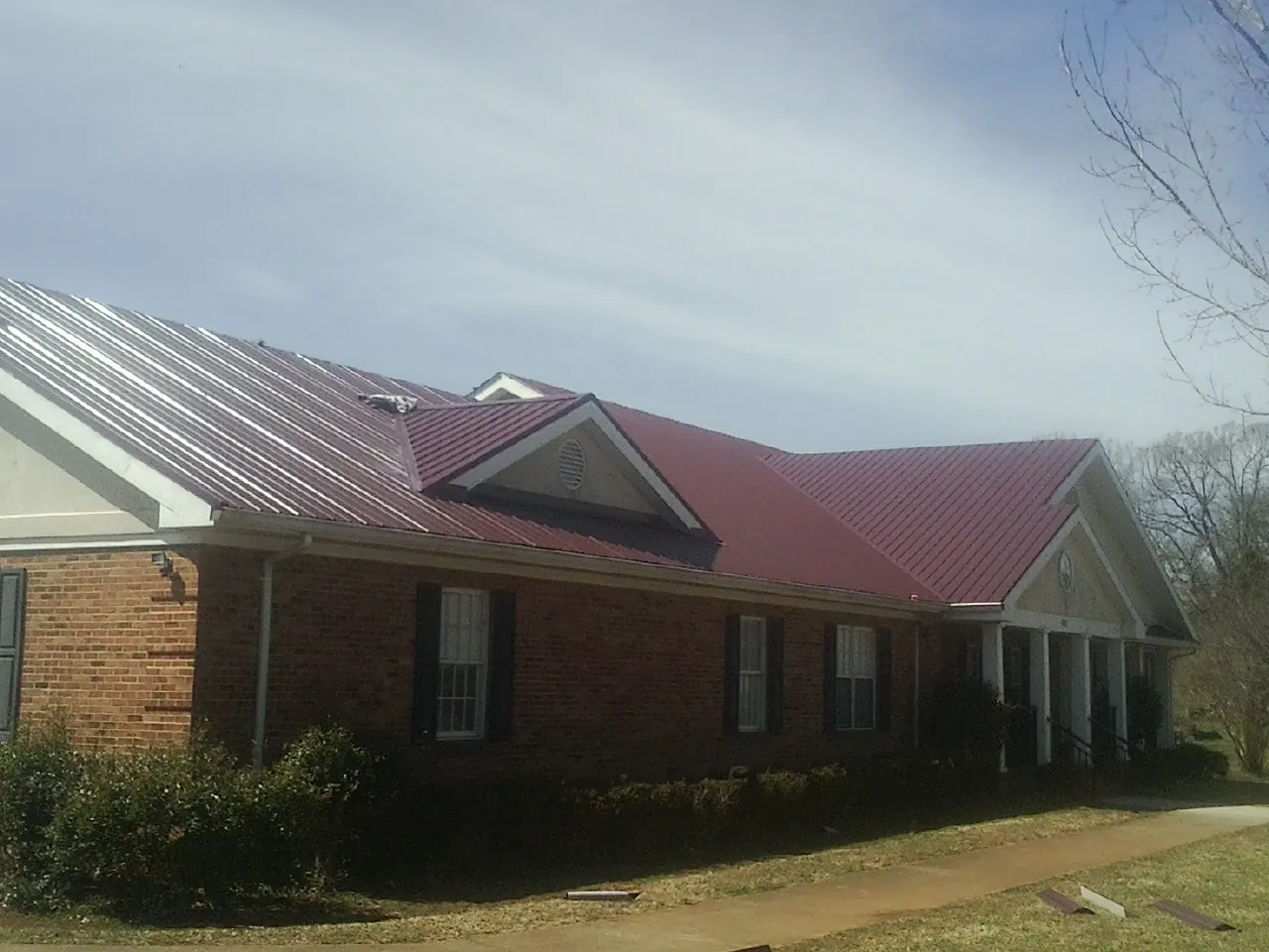 Red metal roof with gabled entries on a long brick building, from a Hail Damage Roof Repair job in Lemoyne