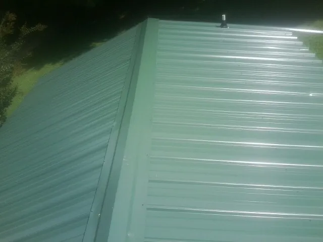 New green metal panels meeting at the ridge of a roof — Flat Roof Repair work by our crew in Lemoyne