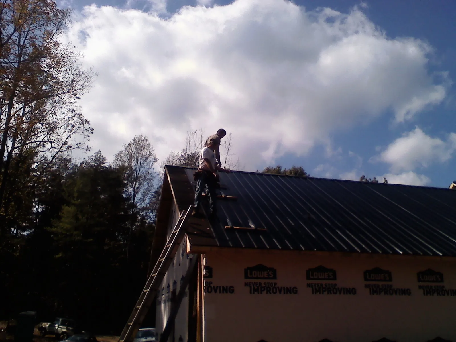 Roofer fastening dark metal panels high against a cloudy sky, from a Roof Inspection job in Lemoyne