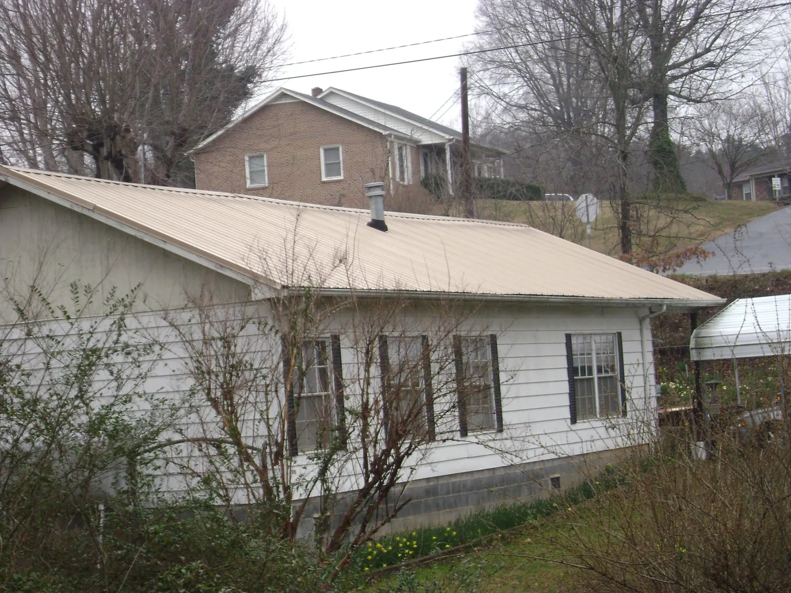 Tan metal roof on a white sided house set into a hillside — Commercial Roofing by Roofing Brothers in Lemoyne